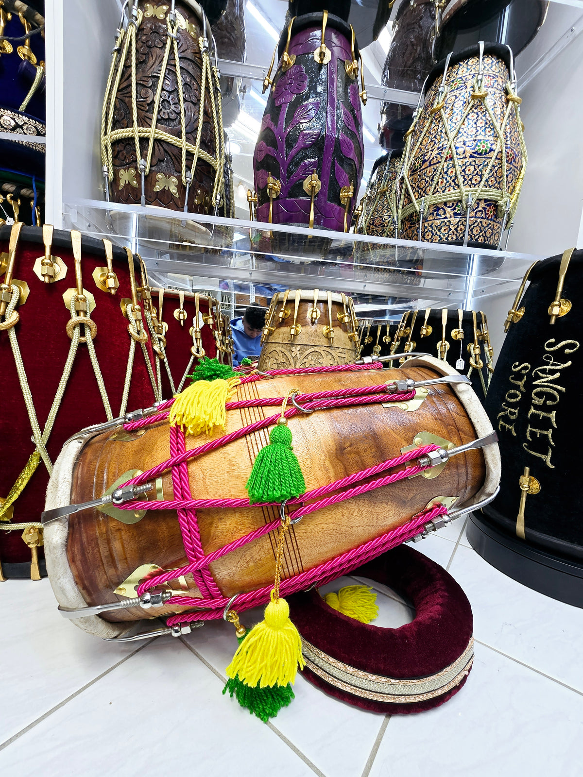 Vibrant Harmony: Chetram Gill's Glossy 2-Tone Red Sheesham Dholak with Chrome Bolts, Pink Ropes Design, and Graceful Green and Yellow Tassels